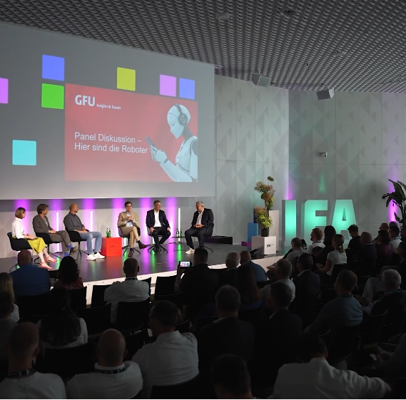 ：论坛现场照片，舞台背景板显示“GFU”标识和德文标题“Panel Diskussion – Hier sind die Roboter”。台上坐着四位嘉宾，台下坐满观众，气氛专注。画面体现IFA作为行业思想交锋前沿阵地的专业氛围。